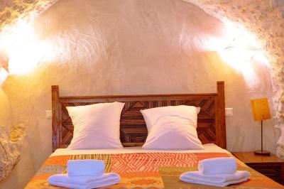 Lit double avec tête de lit en bois sculpté, draps blancs et serviettes pliées, dans une chambre aux murs en pierre.