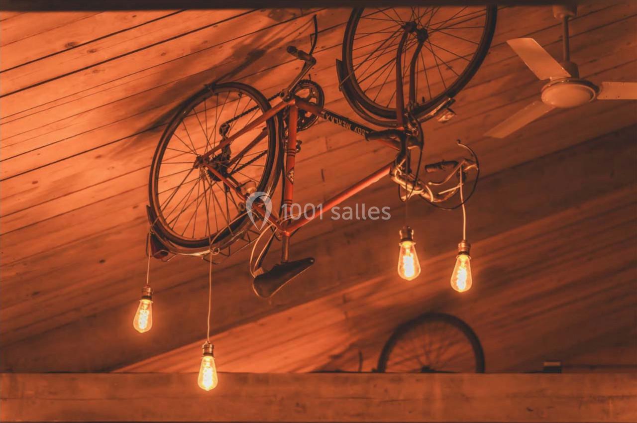 Un vélo suspendu au plafond en bois, entouré d'ampoules suspendues diffusant une lumière chaude.
