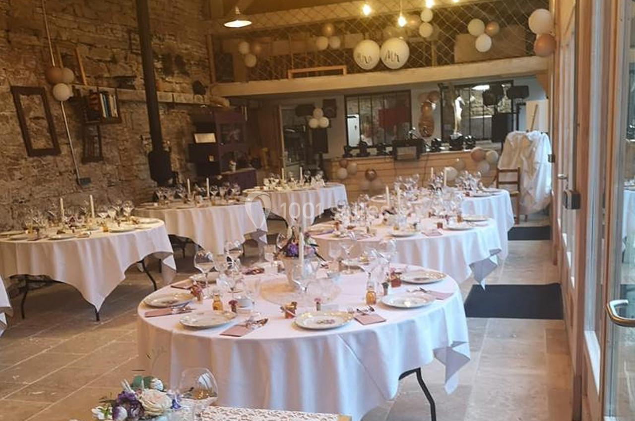Salle de réception décorée avec des tables rondes dressées, ornées de fleurs et de ballons suspendus.