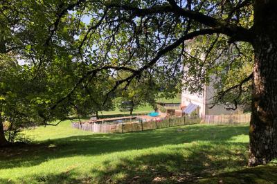 Façade d'une maison beige à volets verts, reflétée dans un bassin entouré de pierres et de végétation.