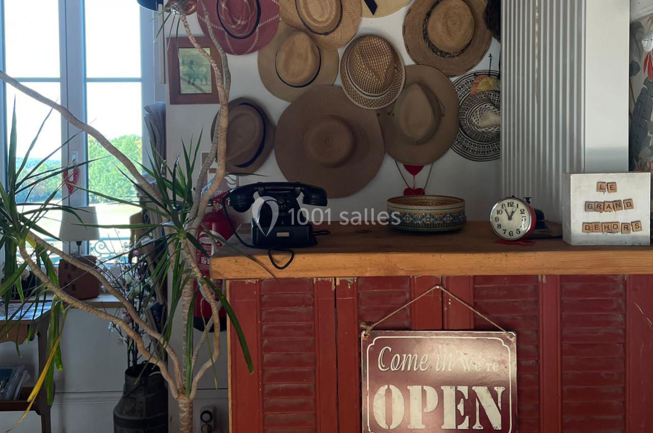 Comptoir en bois décoré de chapeaux, téléphone vintage, horloge et panneau ’Open’, près d'une fenêtre lumineuse.