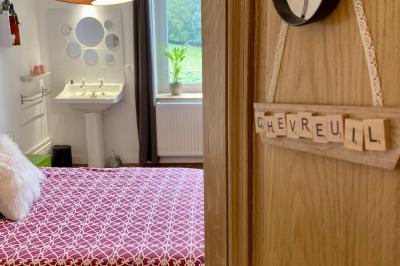 Façade d'une maison beige à volets verts, reflétée dans un bassin entouré de pierres et de végétation.