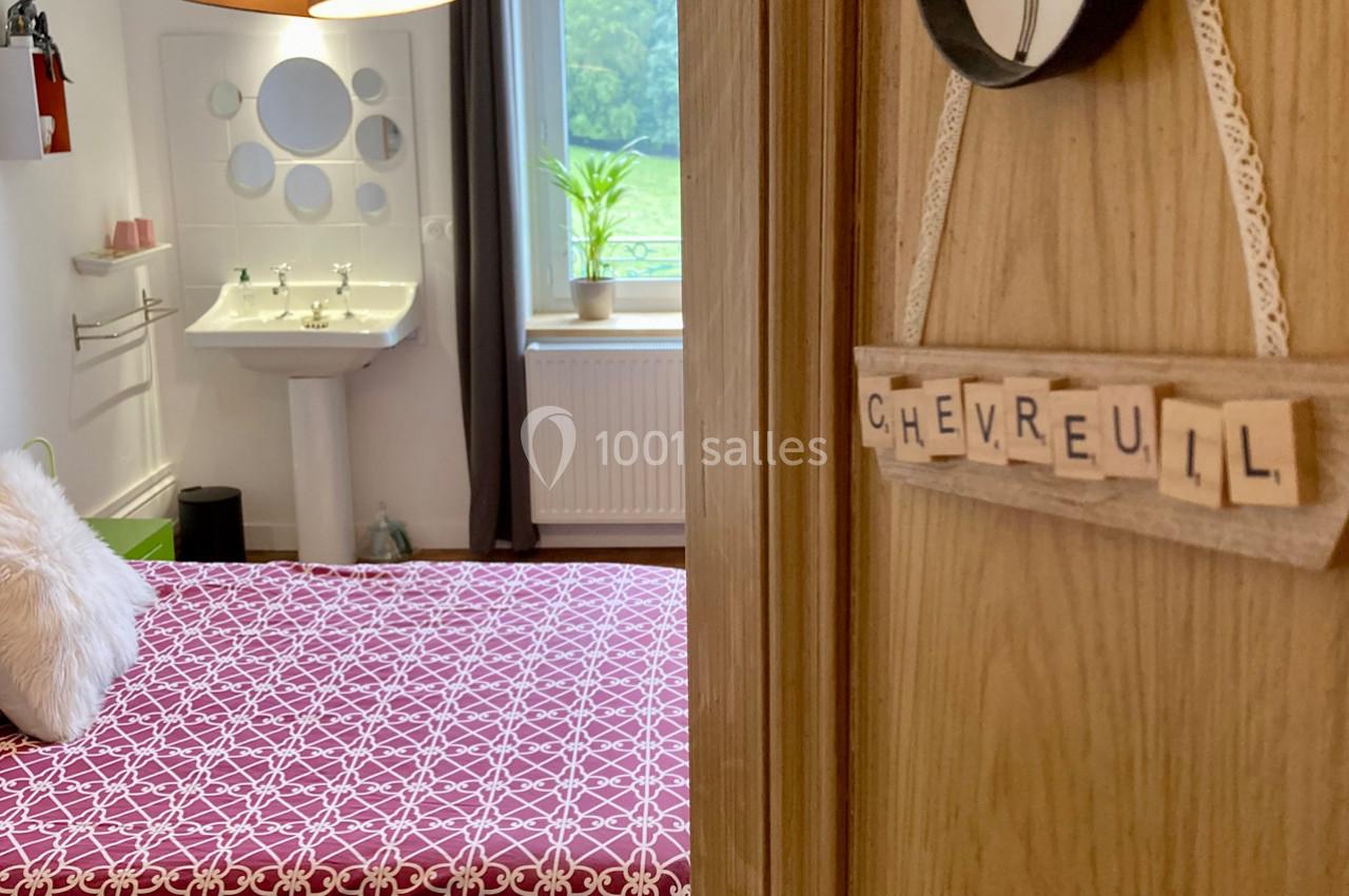 Vue d'une chambre avec un lit à motif géométrique, un lavabo, une fenêtre et une pancarte ’Chevreuil’ sur la porte.