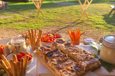 Façade d'une maison beige à volets verts, reflétée dans un bassin entouré de pierres et de végétation.