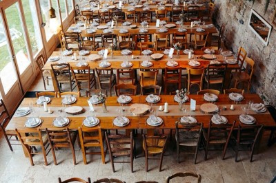 Façade d'une maison beige à volets verts, reflétée dans un bassin entouré de pierres et de végétation.