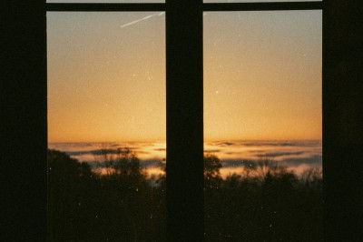 Façade d'une maison beige à volets verts, reflétée dans un bassin entouré de pierres et de végétation.