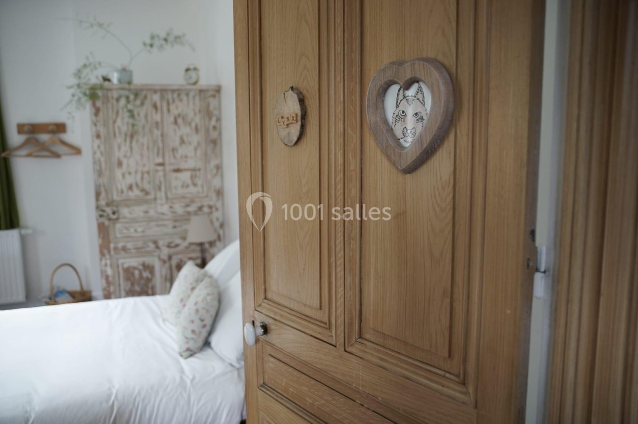 Porte en bois avec des décorations murales en forme de cœur, donnant sur une chambre lumineuse avec un lit et une armoire…
