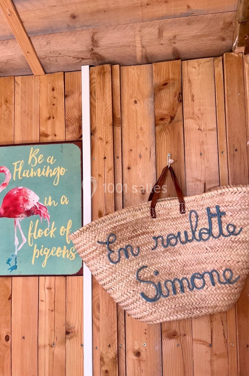 Panneau avec un flamant rose et un panier en osier suspendu, inscrit ’En route Simone’, sur un mur en bois.