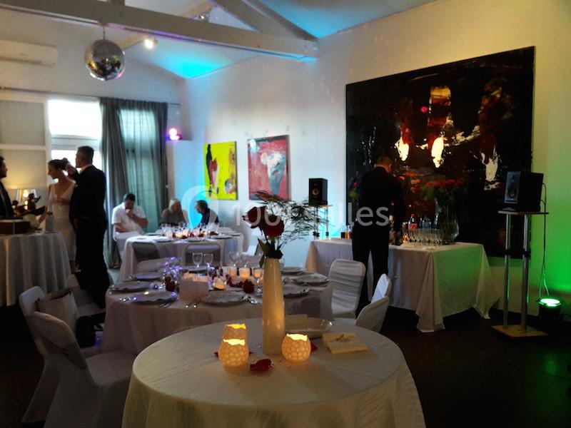 Salle décorée pour un événement avec tables dressées, éclairage tamisé et œuvres d'art accrochées aux murs.