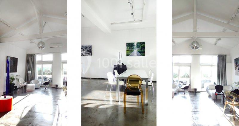 Salle lumineuse avec de grandes fenêtres, mobilier moderne et œuvres d'art accrochées aux murs blancs.