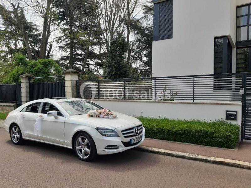 Voiture blanche décorée de fleurs garée devant une maison moderne avec jardin et clôture en métal.