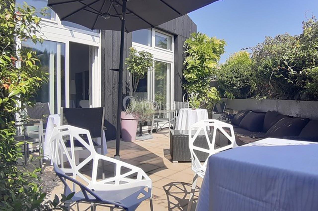 Terrasse ensoleillée avec mobilier moderne, parasol noir, plantes et baies vitrées donnant sur l'intérieur.