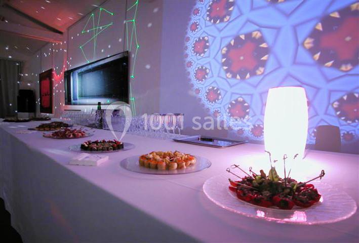 Table dressée avec des amuse-bouches, verres et décorations lumineuses projetées sur les murs.