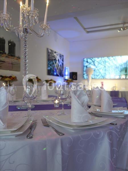 Table dressée avec nappes blanches, serviettes pliées, chandeliers et verres, dans une salle décorée et éclairée.