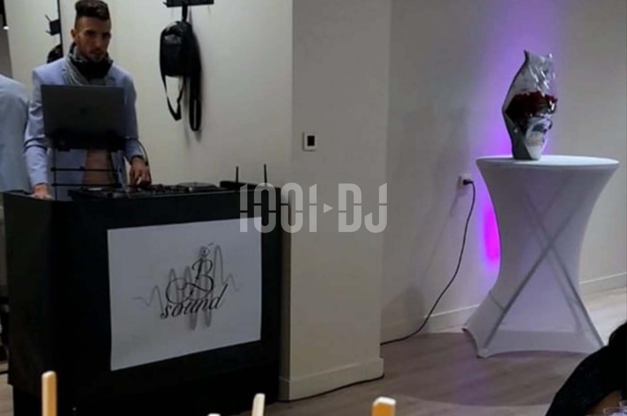 Un DJ mixe derrière une table de sonorisation dans une salle éclairée, avec une table haute décorative à côté.