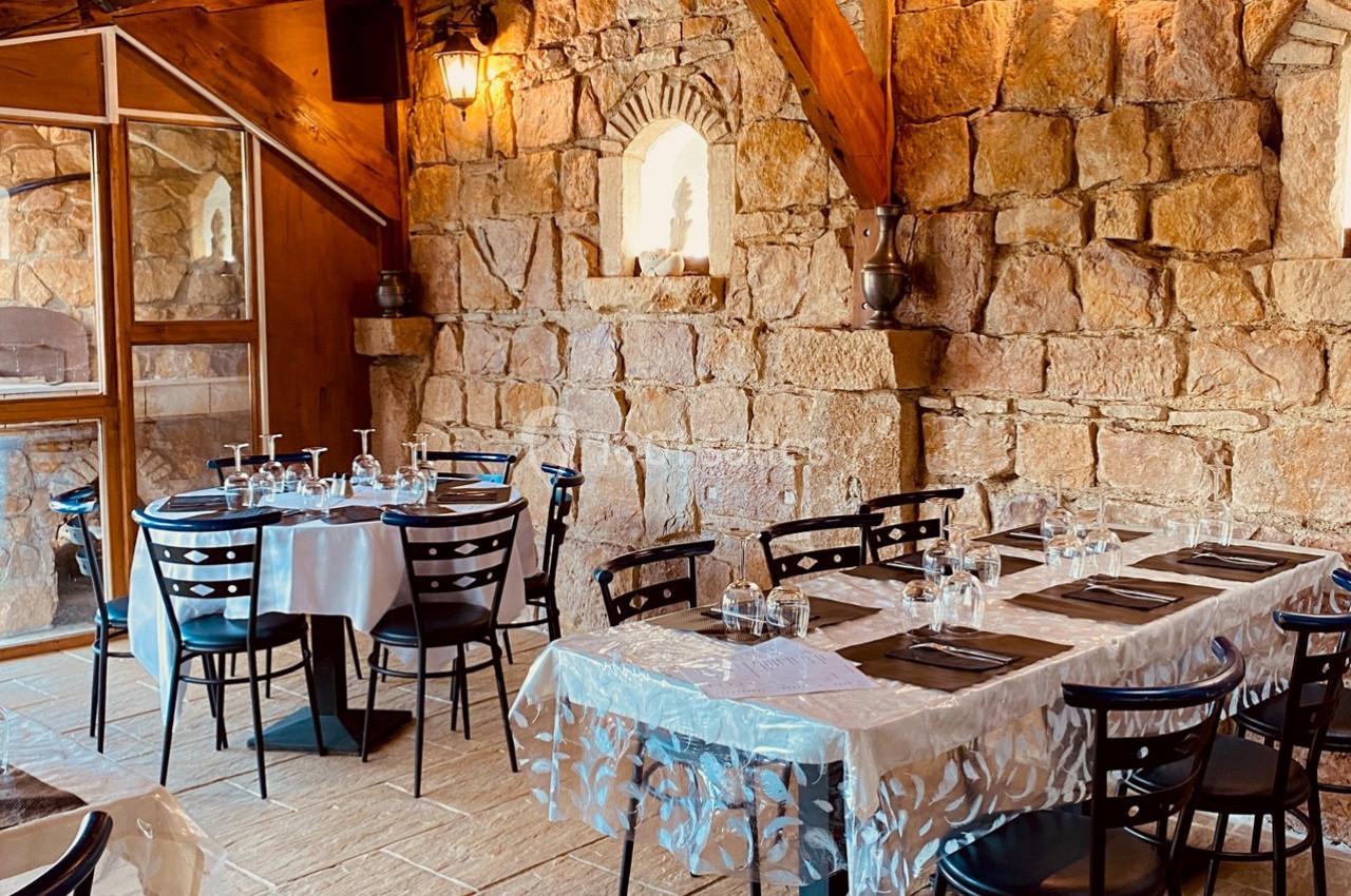 Salle de restaurant avec murs en pierre, tables dressées avec nappes blanches et chaises noires, ambiance chaleureuse.