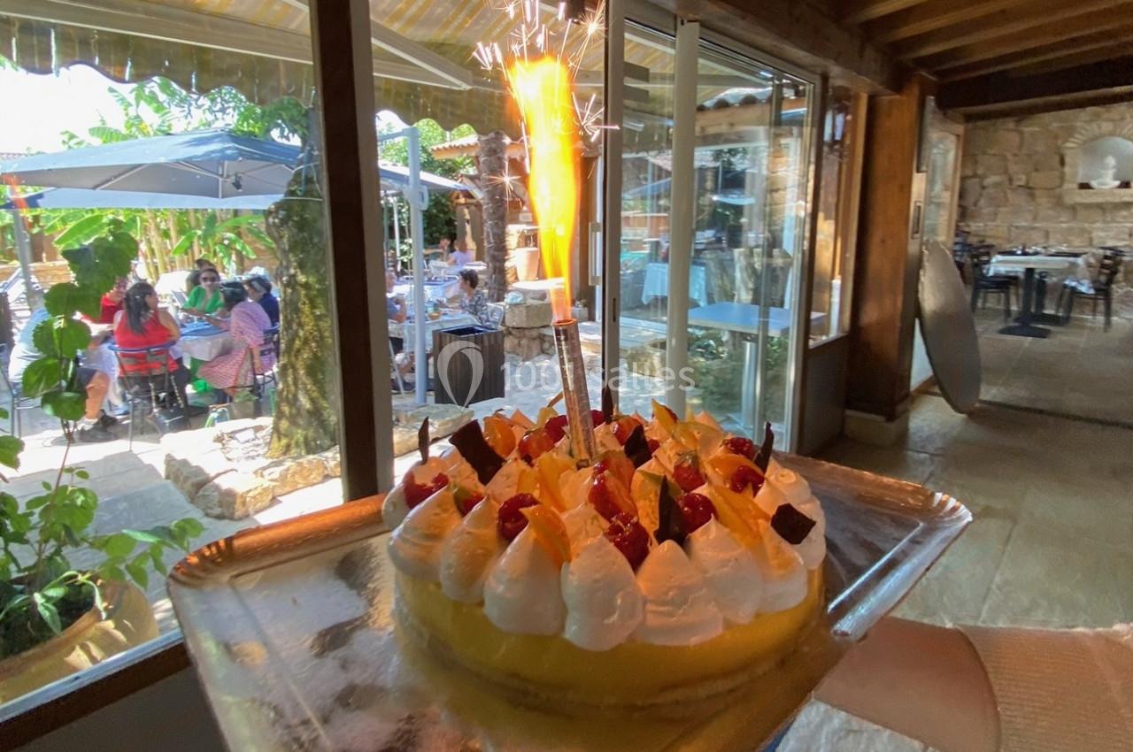 Gâteau décoré de fruits et de crème avec une bougie étincelante, présenté dans un restaurant lumineux.
