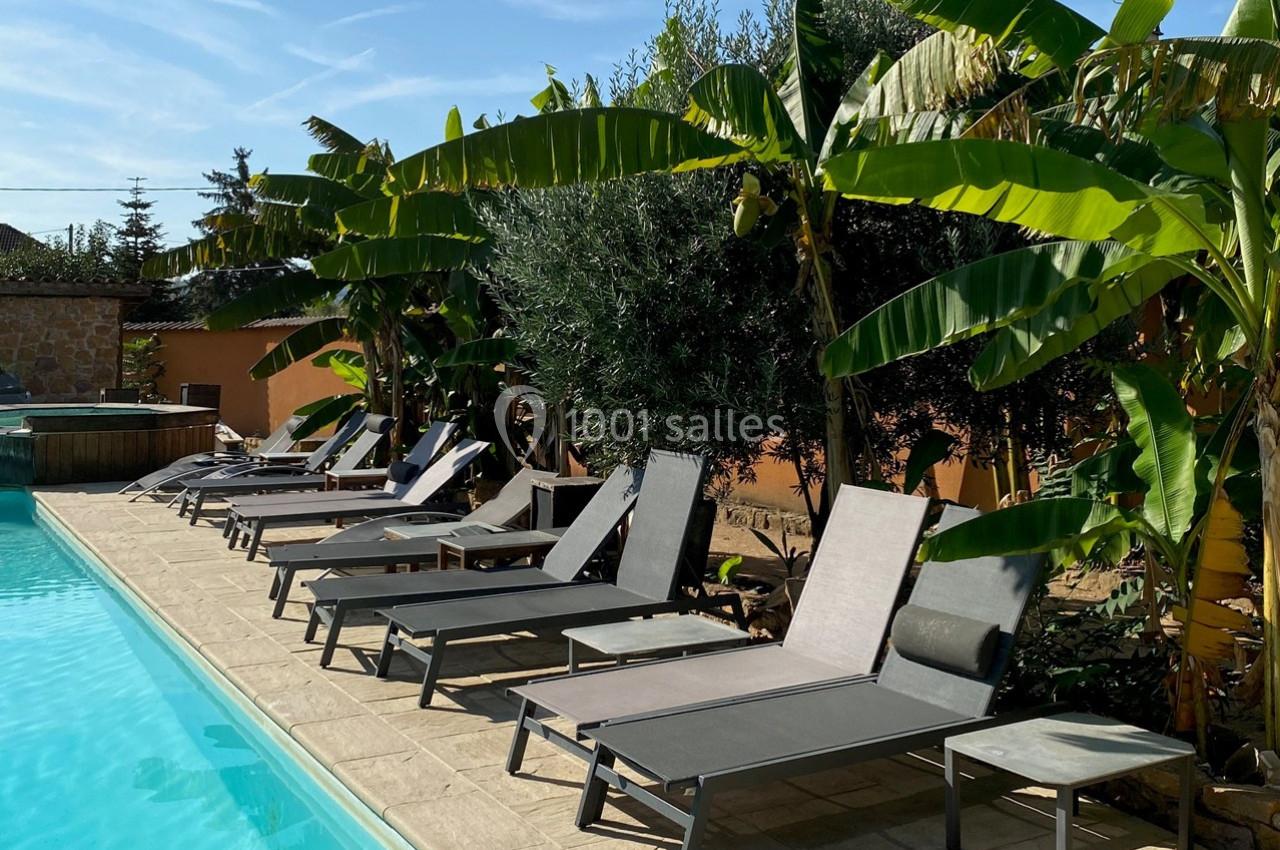 Transats alignés le long d'une piscine entourée de végétation tropicale avec des bananiers en arrière-plan.