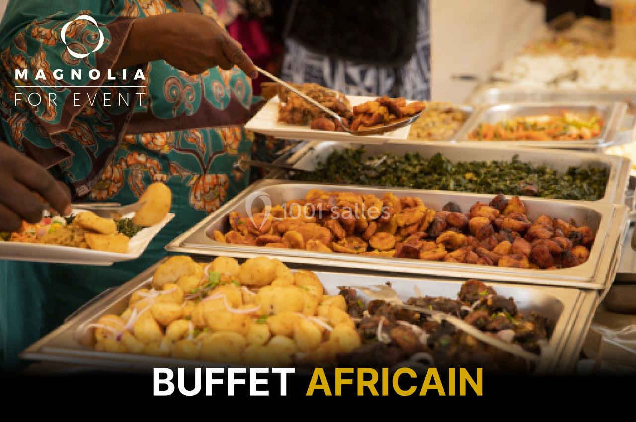 Buffet composé de plats africains variés, incluant beignets, légumes sautés et brochettes, présenté sur des plateaux.