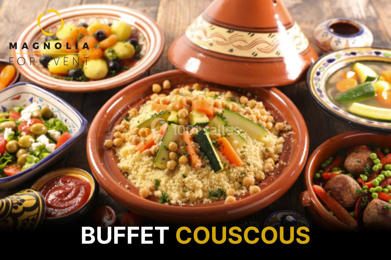 Plat de couscous garni de légumes et pois chiches, entouré d'autres plats colorés sur une table en bois.