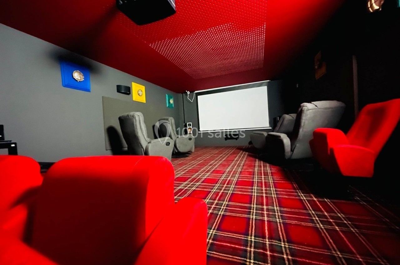 Salle de cinéma privée avec fauteuils rouges et gris, écran blanc et plafond rouge perforé.