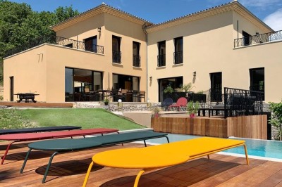 Piscine à débordement entourée de transats colorés sur une terrasse en bois, avec vue sur une campagne vallonnée.