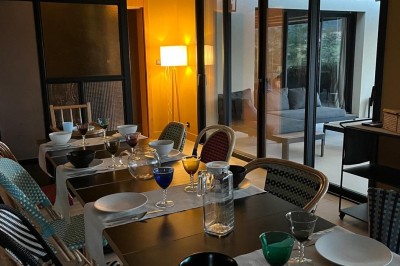 Piscine à débordement entourée de transats colorés sur une terrasse en bois, avec vue sur une campagne vallonnée.