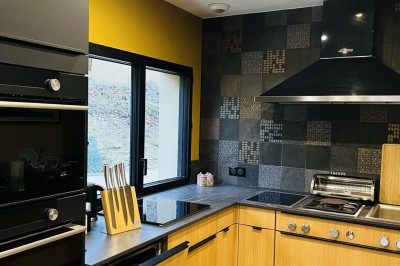 Piscine à débordement entourée de transats colorés sur une terrasse en bois, avec vue sur une campagne vallonnée.