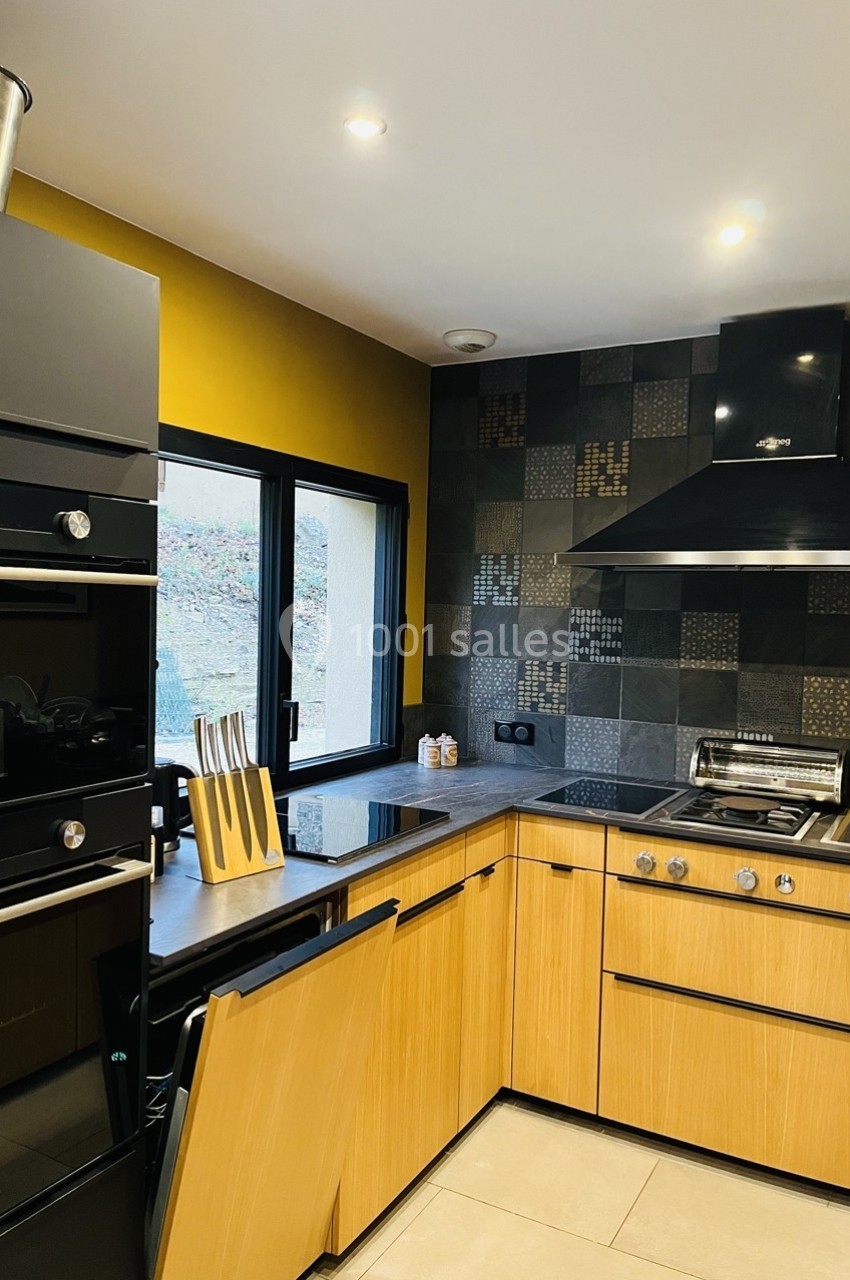 Cuisine moderne avec meubles en bois clair, plan de travail sombre, crédence en carreaux noirs et électroménagers intégrés.