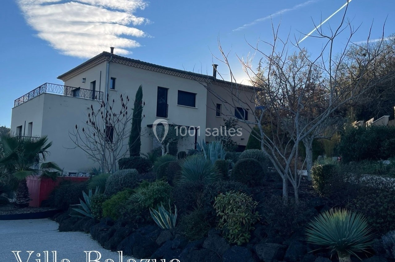Vue d'une villa moderne entourée d'un jardin arboré et de végétation méditerranéenne sous un ciel dégagé.