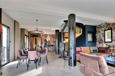 Piscine à débordement entourée de transats colorés sur une terrasse en bois, avec vue sur une campagne vallonnée.