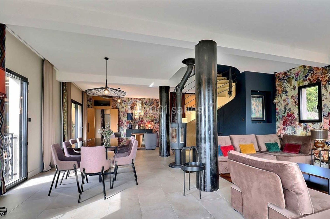 Salon moderne avec canapé, table à manger, escalier en colimaçon et murs décorés de motifs colorés.