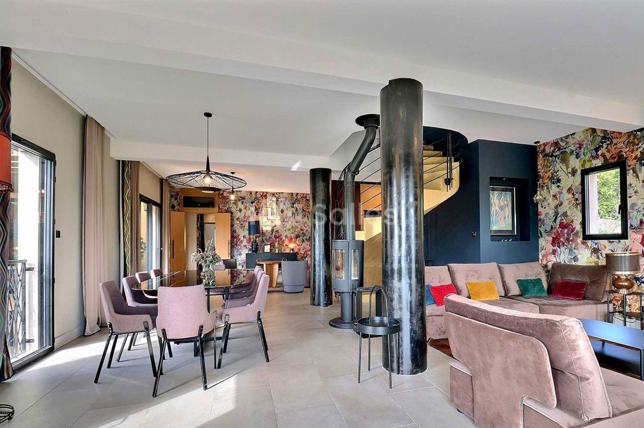 Salon moderne avec canapé, table à manger, escalier en colimaçon et murs décorés de motifs colorés.