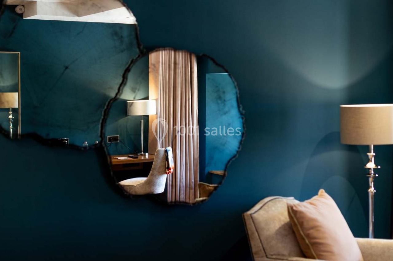 Reflet d'une lampe, d'un fauteuil et d'un rideau beige dans deux miroirs ronds sur un mur bleu.