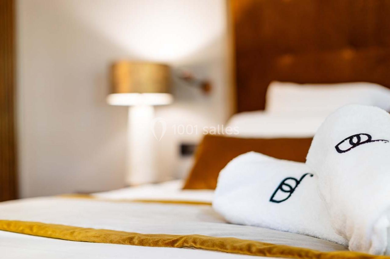 Lit avec des draps blancs, serviettes pliées et lampe de chevet allumée dans une chambre chaleureuse.