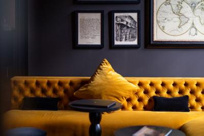 Canapé jaune moutarde capitonné avec coussins noirs, tables basses noires et cadres décoratifs accrochés au mur sombre.