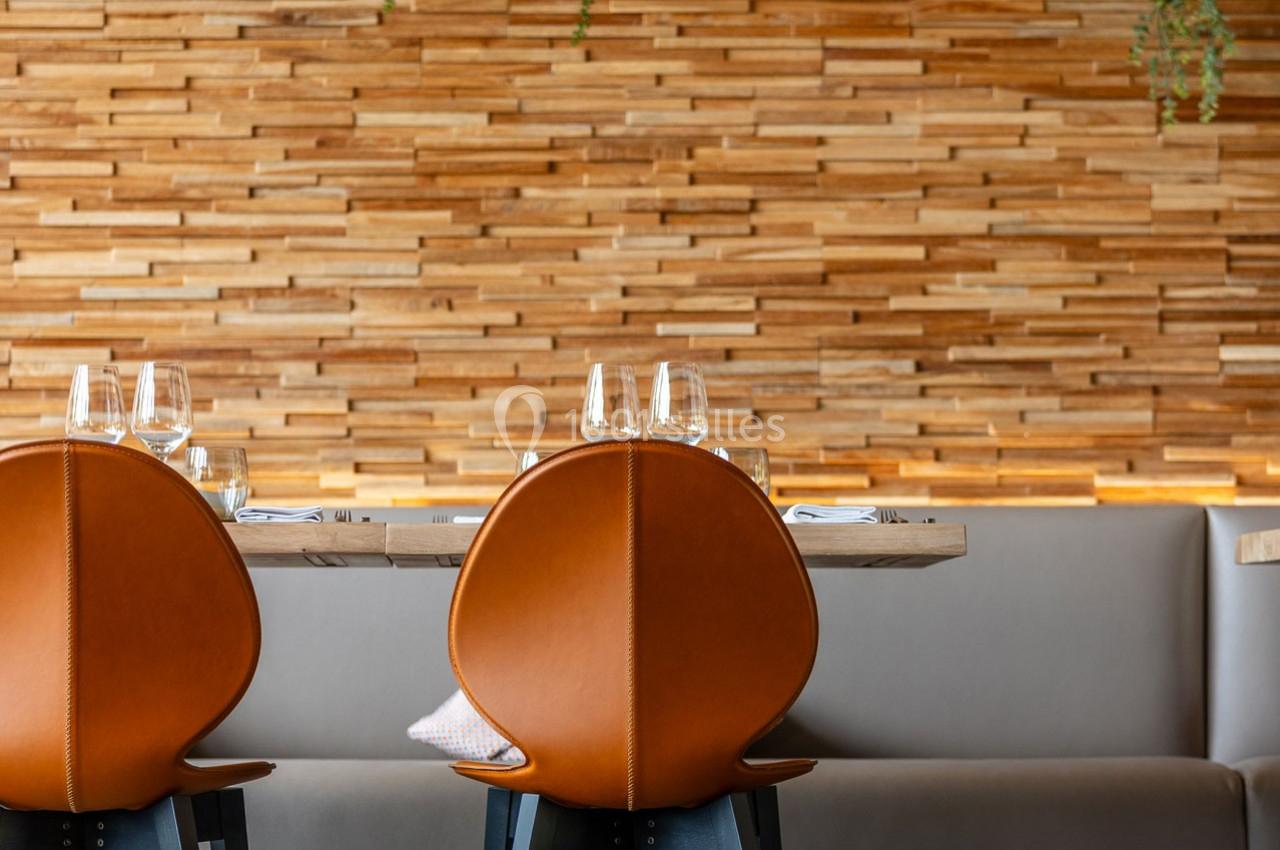 Deux chaises en cuir orange devant une table dressée, avec un mur en bois texturé en arrière-plan.