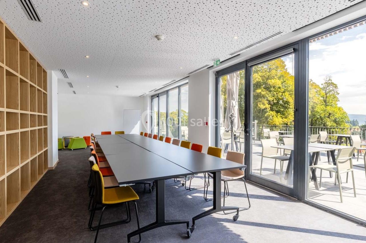 Salle de réunion lumineuse avec une grande table, des chaises colorées et accès à une terrasse extérieure.