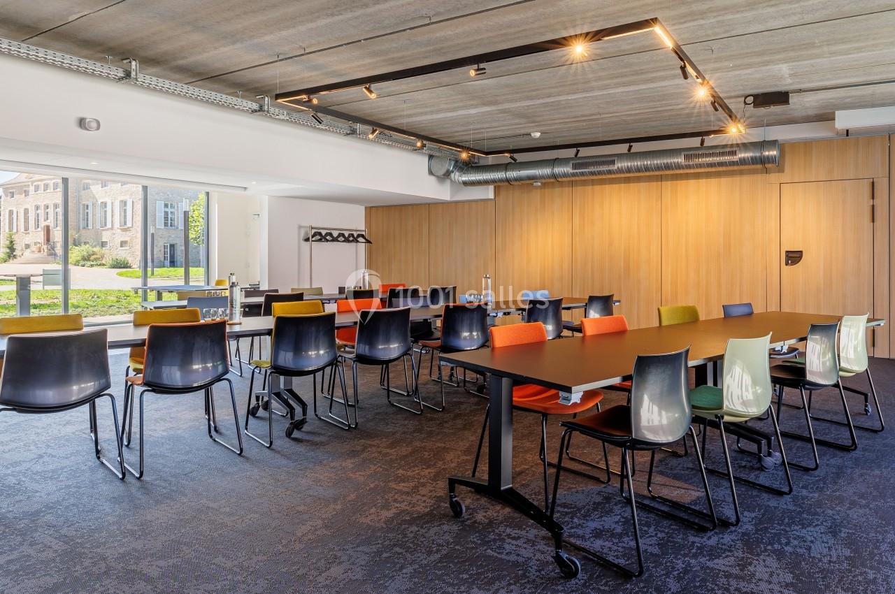Salle de réunion moderne avec grandes tables noires, chaises colorées et vue sur un bâtiment historique à travers les…