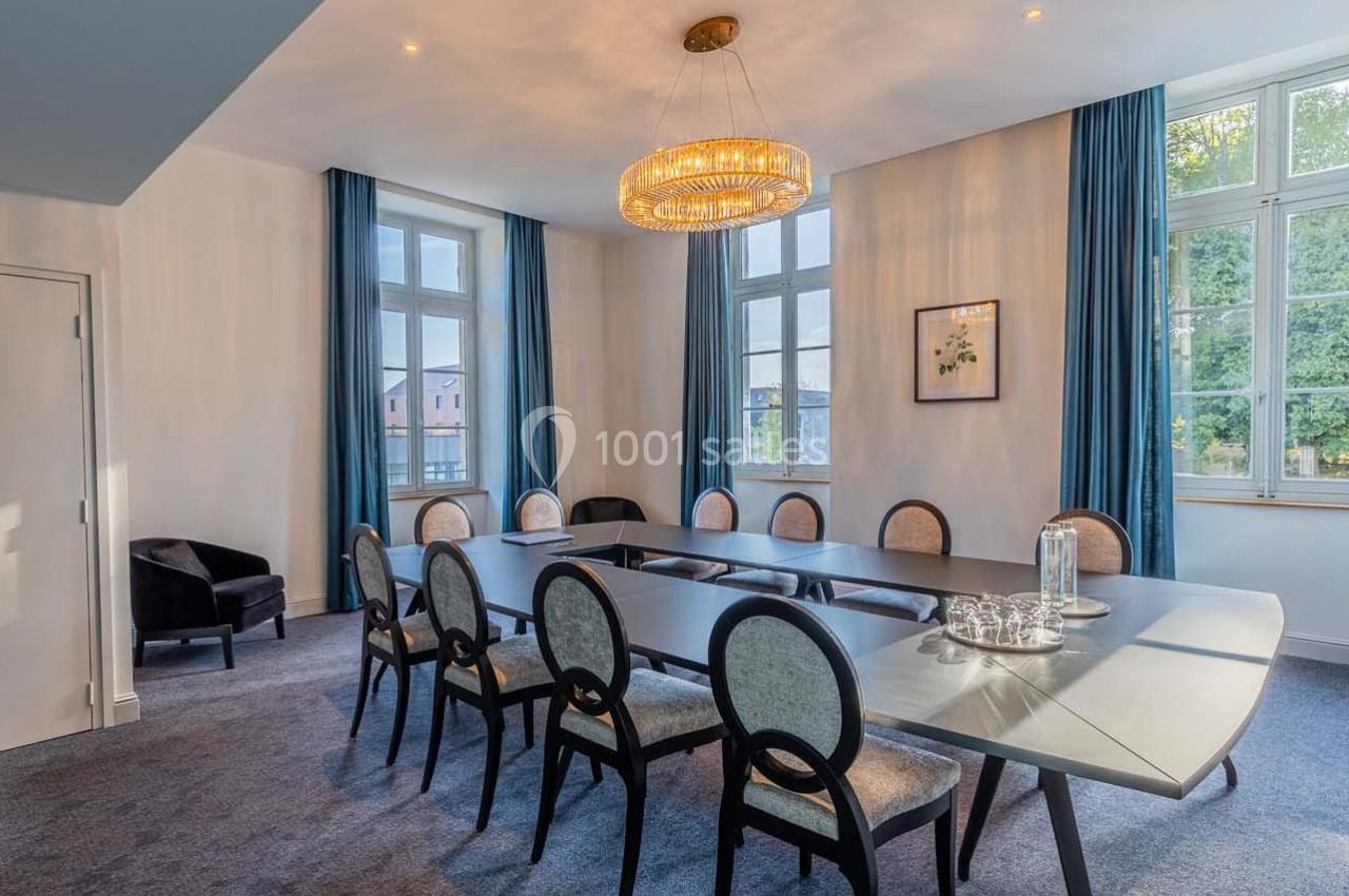 Salle de réunion lumineuse avec grande table ovale, chaises élégantes, lustre moderne et fenêtres donnant sur un extérieur…