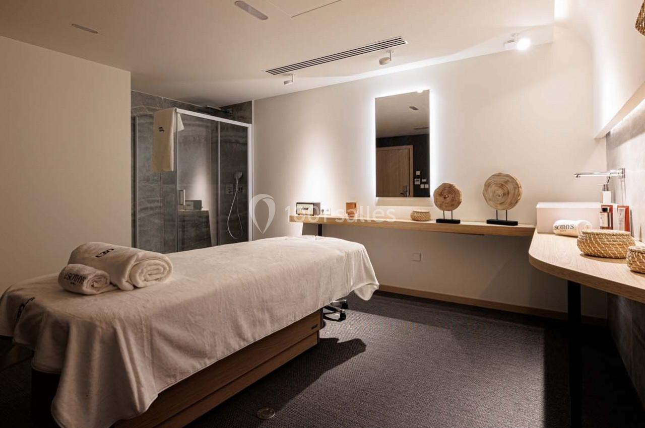 Salle de massage avec table recouverte de serviettes blanches, éclairage doux et décoration minimaliste.