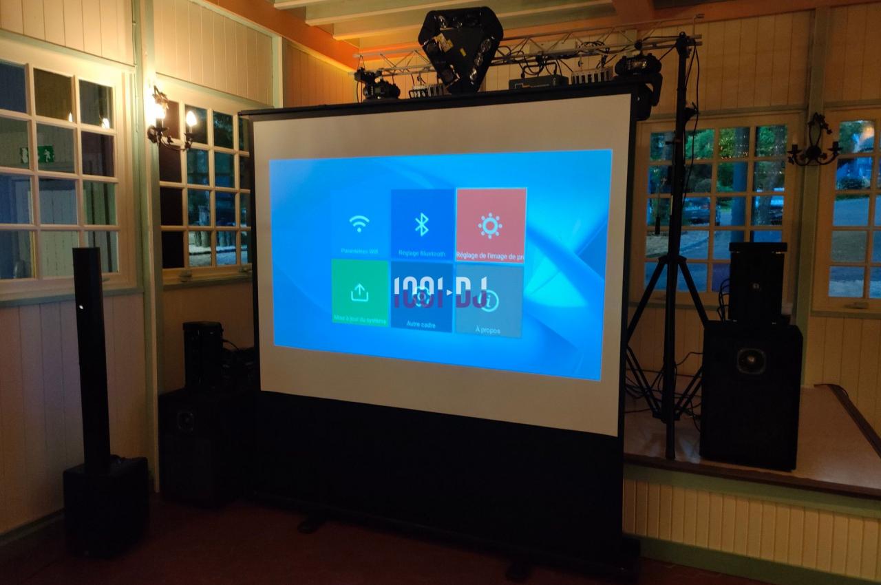Écran de projection affichant une interface numérique, entouré de matériel audio dans une salle éclairée.