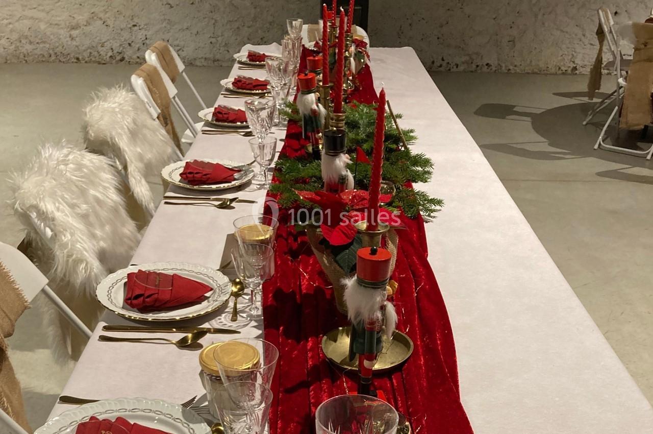 Table décorée pour un repas festif avec nappe rouge, bougies, poinsettias et assiettes dressées.