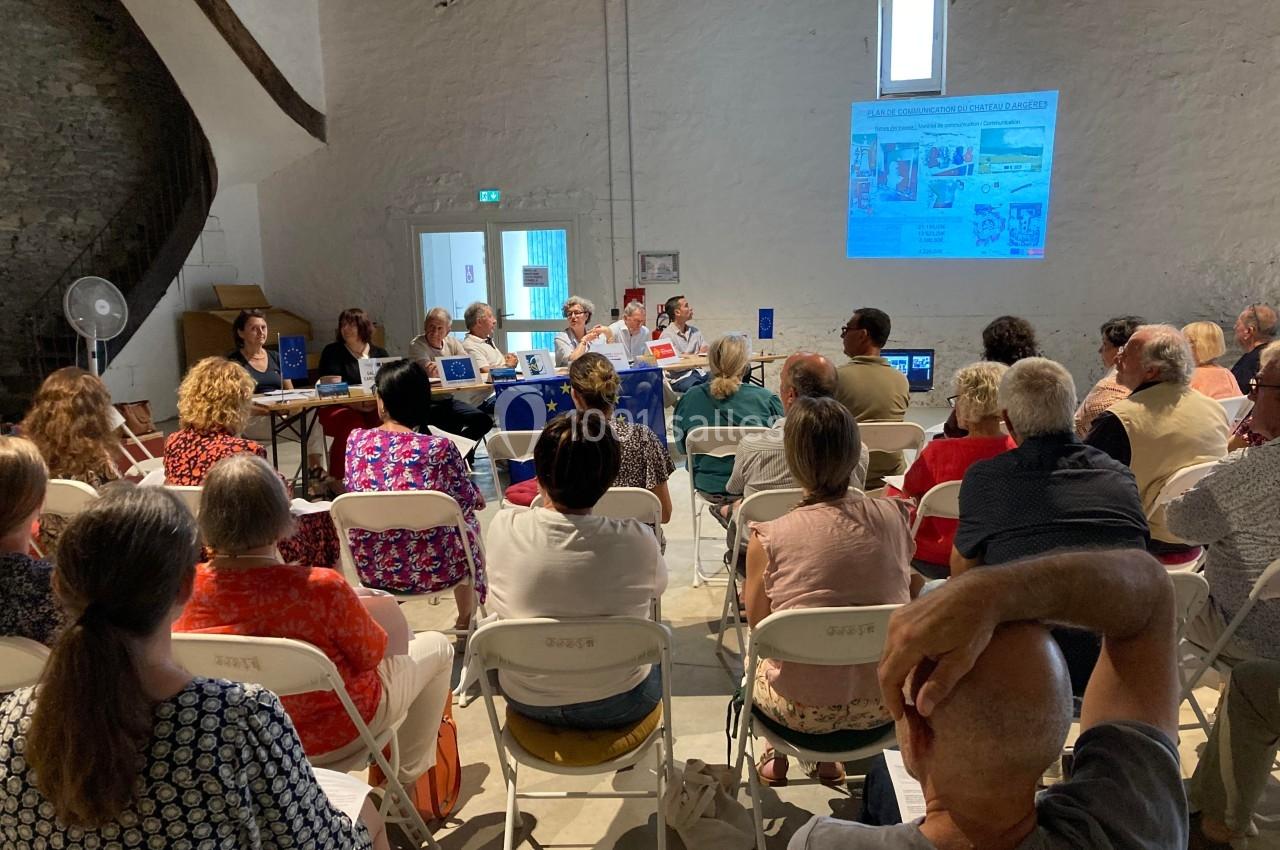 Un groupe de personnes assises assiste à une présentation dans une salle avec un écran projetant des images.