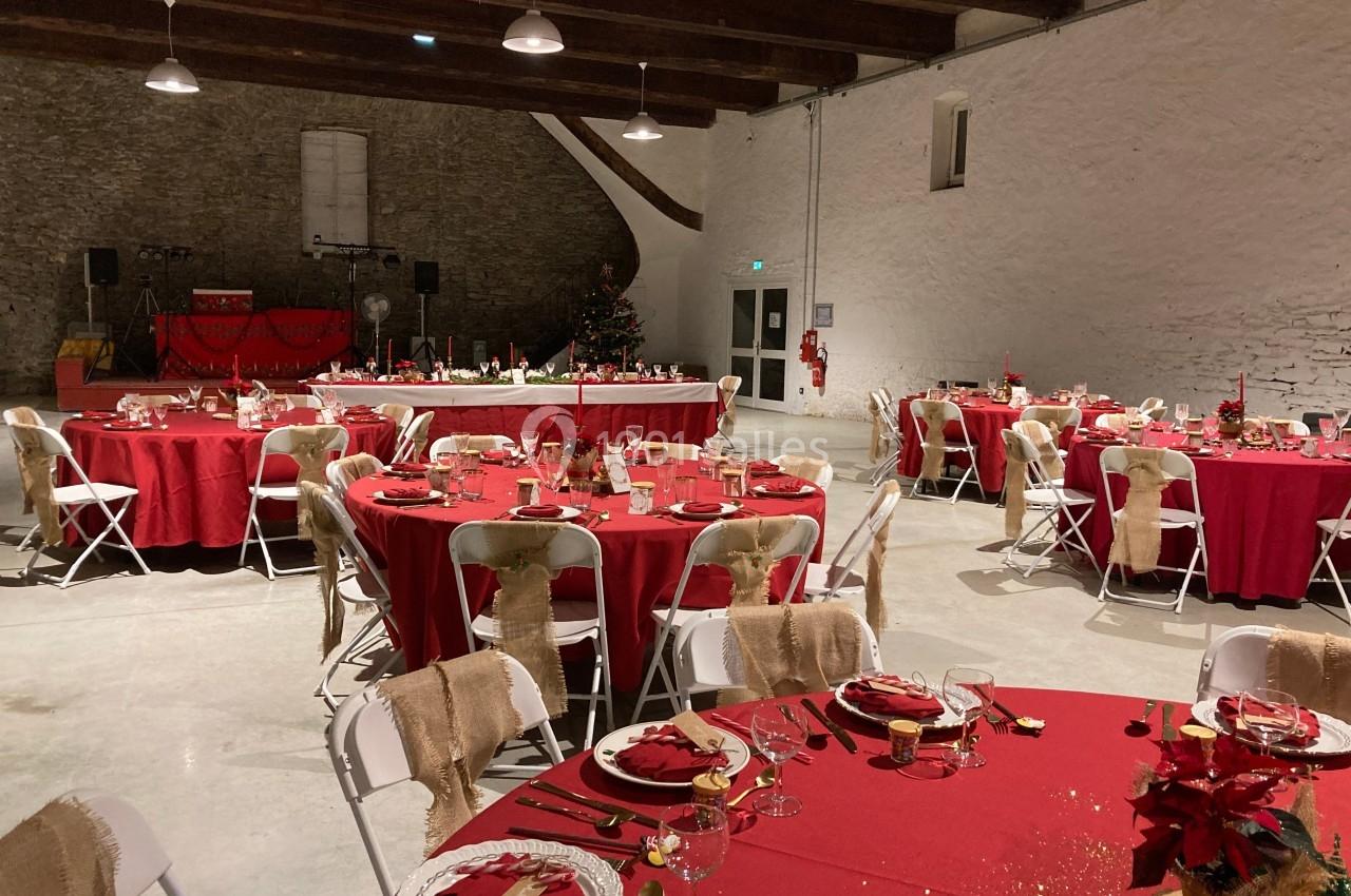 Salle de réception décorée pour un événement, avec des tables rondes dressées de nappes rouges et des chaises blanches.