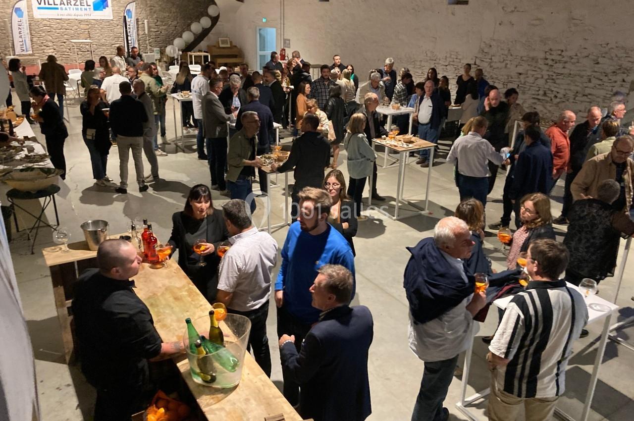 Groupe de personnes échangeant et dégustant des boissons dans une salle avec des murs en pierre et des stands.