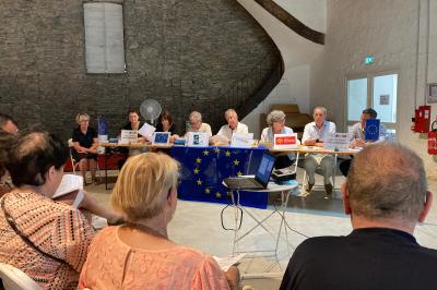 Des personnes assises dans une salle assistent à une présentation projetée sur un mur, avec documents en main.