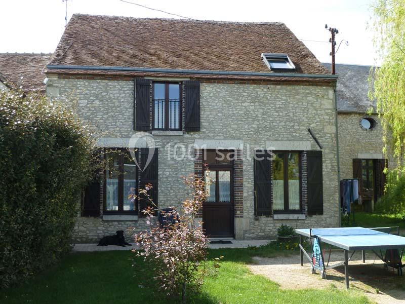 Façade d'une maison en pierre avec volets en bois, jardin verdoyant et table de ping-pong au premier plan.