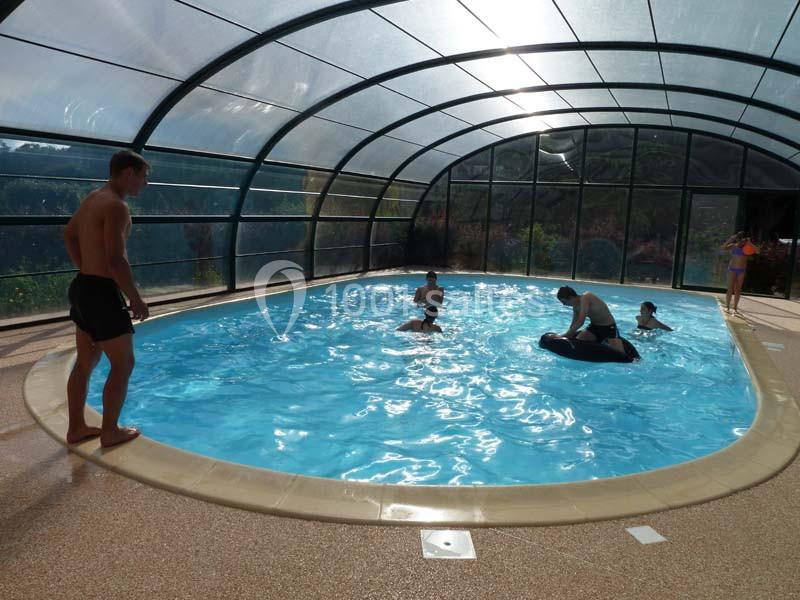 Piscine couverte avec plusieurs personnes nageant ou jouant dans l'eau sous une structure vitrée.