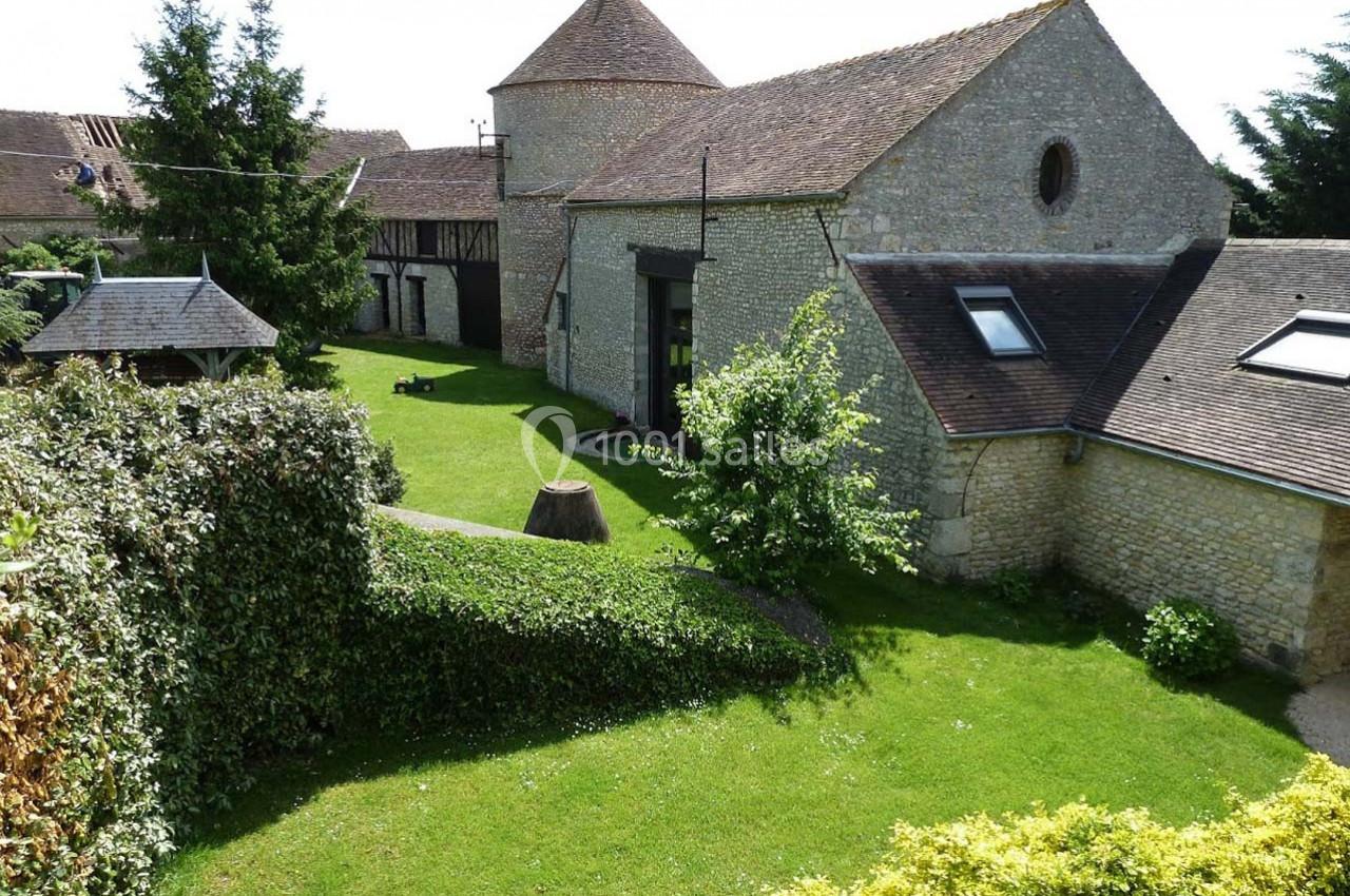 Bâtiments en pierre avec toits en tuiles entourés d'un jardin verdoyant et arboré sous un ciel clair.